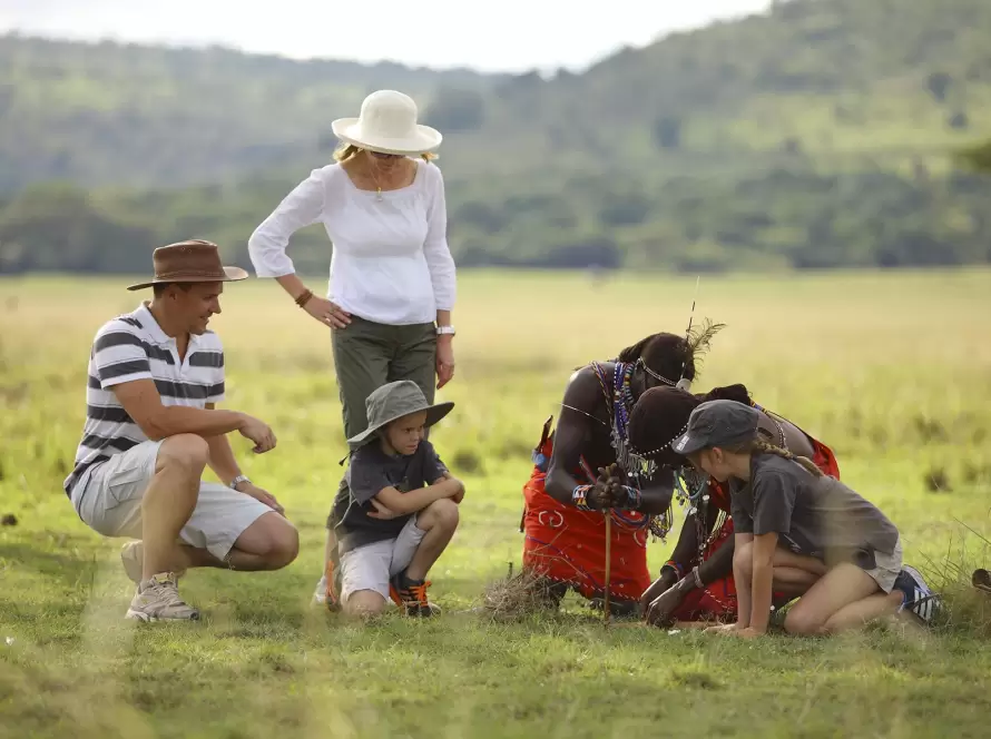 Family African safari experience with children learning traditional skills from a Maasai guide in the wilderness.