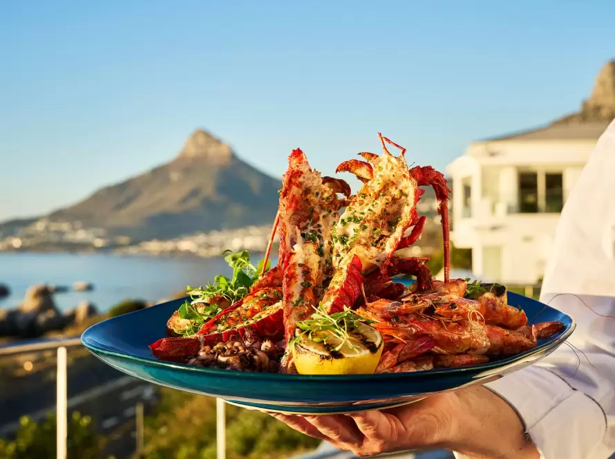 Cape Town’s luxurious South African cuisine features grilled seafood with Table Mountain in the backdrop.