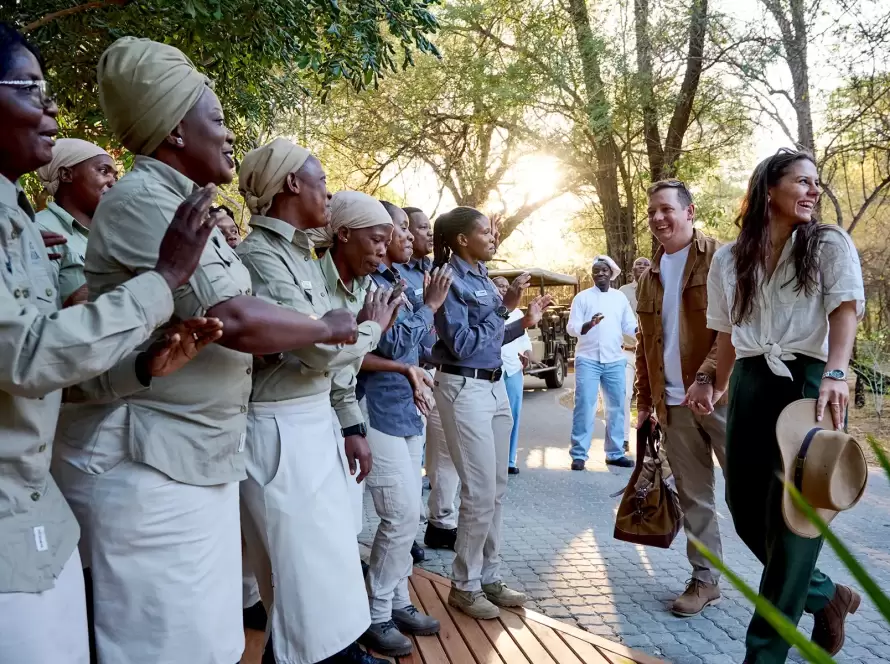 A couple on a romantic African safari, carrying a duffle bag, being welcomed at a luxury African lodge.