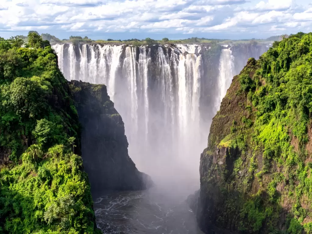 Majestic Victoria Falls in Zimbabwe, one of the world’s largest and most breathtaking waterfalls, cascading into the Zambezi River gorge with lush greenery surrounding it.