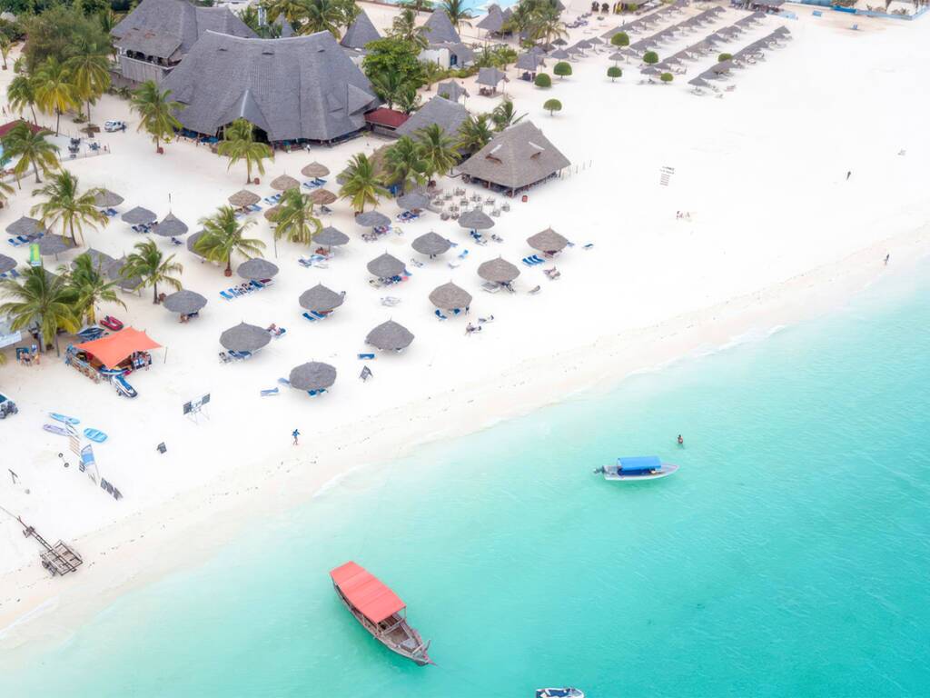 Kendwa Beach in Zanzibar, lined with palm trees, beach umbrellas, and crystal-clear waters, with boats.