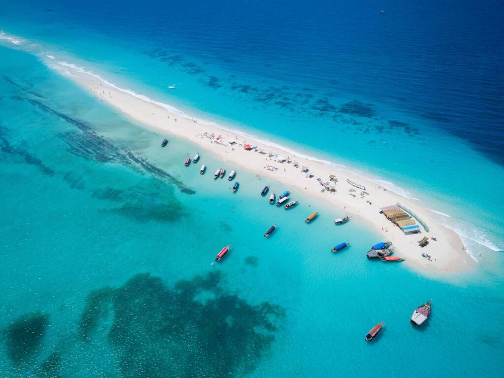 Nakupenda Beach in Zanzibar with white sands surrounded by crystal-clear turquoise waters, with boats. 