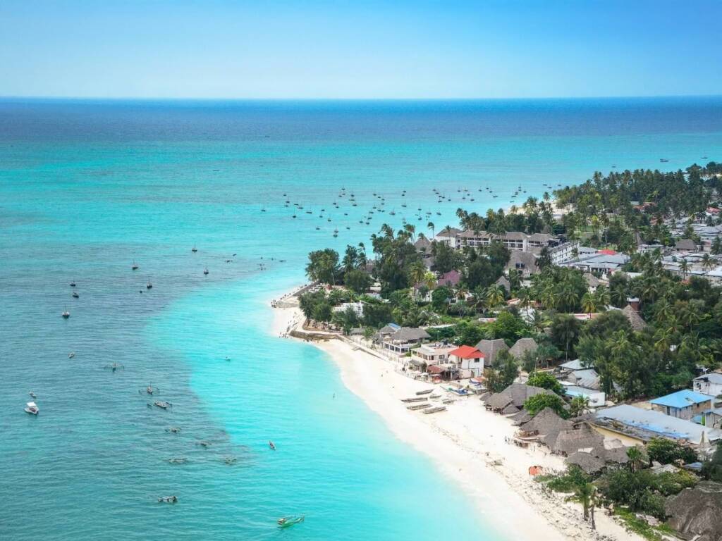 Nungwi Beach with clear turquoise waters, boats and lively beachfront hotels in Zanzibar.
