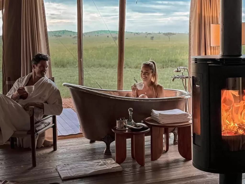 Newlyweds’ private moments in a romantic bathtub in a luxury safari tent with a fireplace nearby.