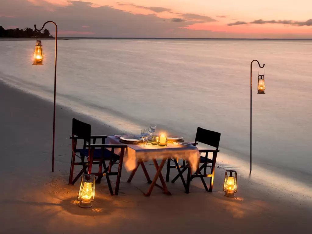 A private and romantic, lantern-lit dinner set-up under a sunset sky on a sandy beach during a luxury Mozambique holiday