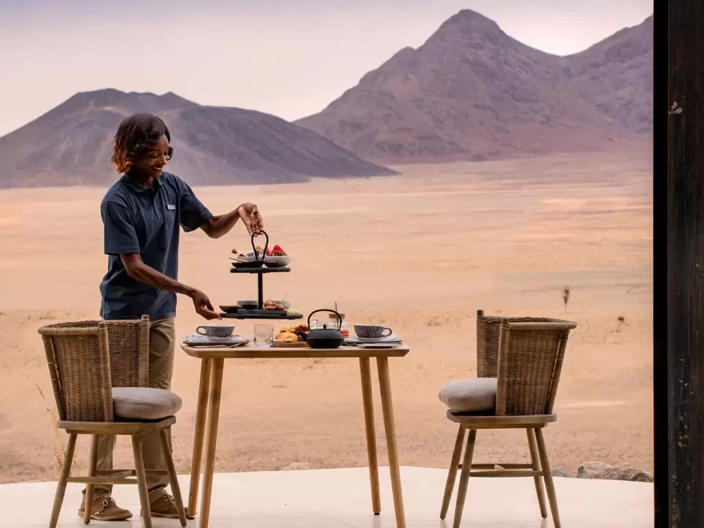 Romantic desert dining setup against the rugged backdrop of Naukluft Mountains during a luxury African safari in Namibia.