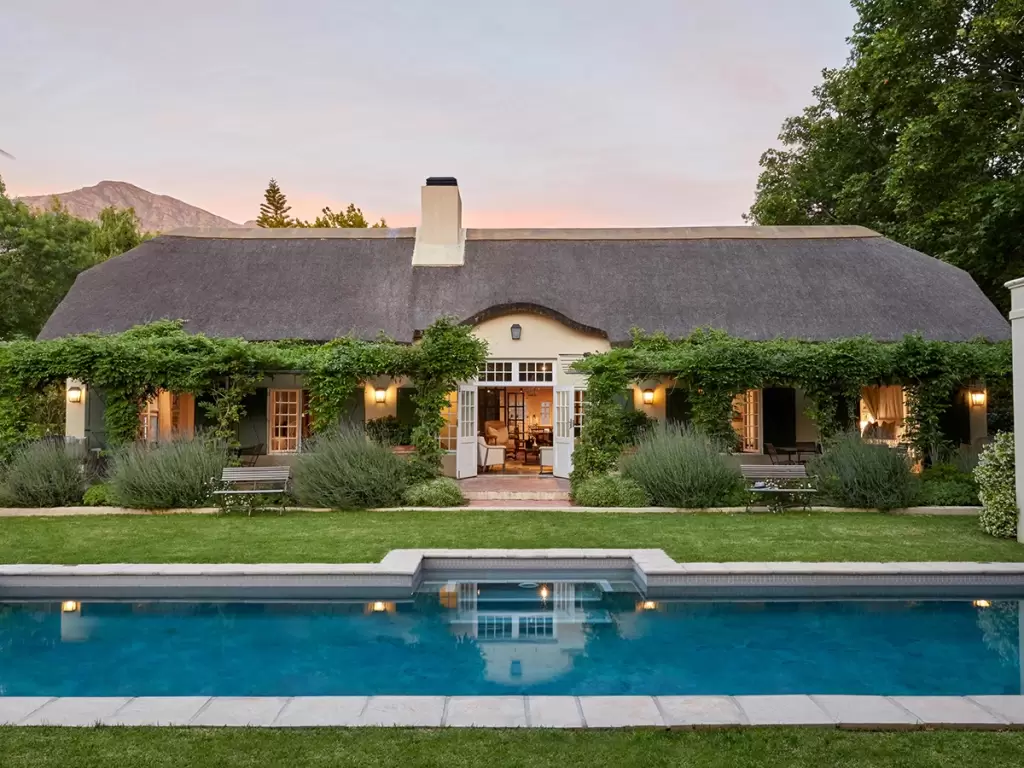 A vintage-style luxury lodge in Cape Winelands’ Franschhoek in South Africa, featuring lush greenery and a sparkling pool at sunset.