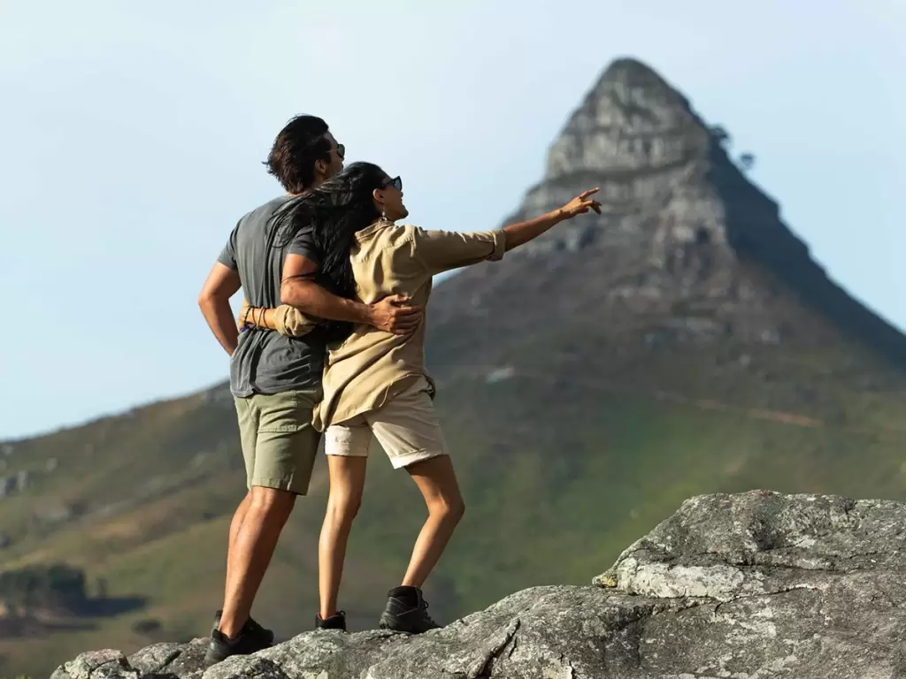 A couple standing together on rocky heights above Cape Town watching the Table Mountain views. 