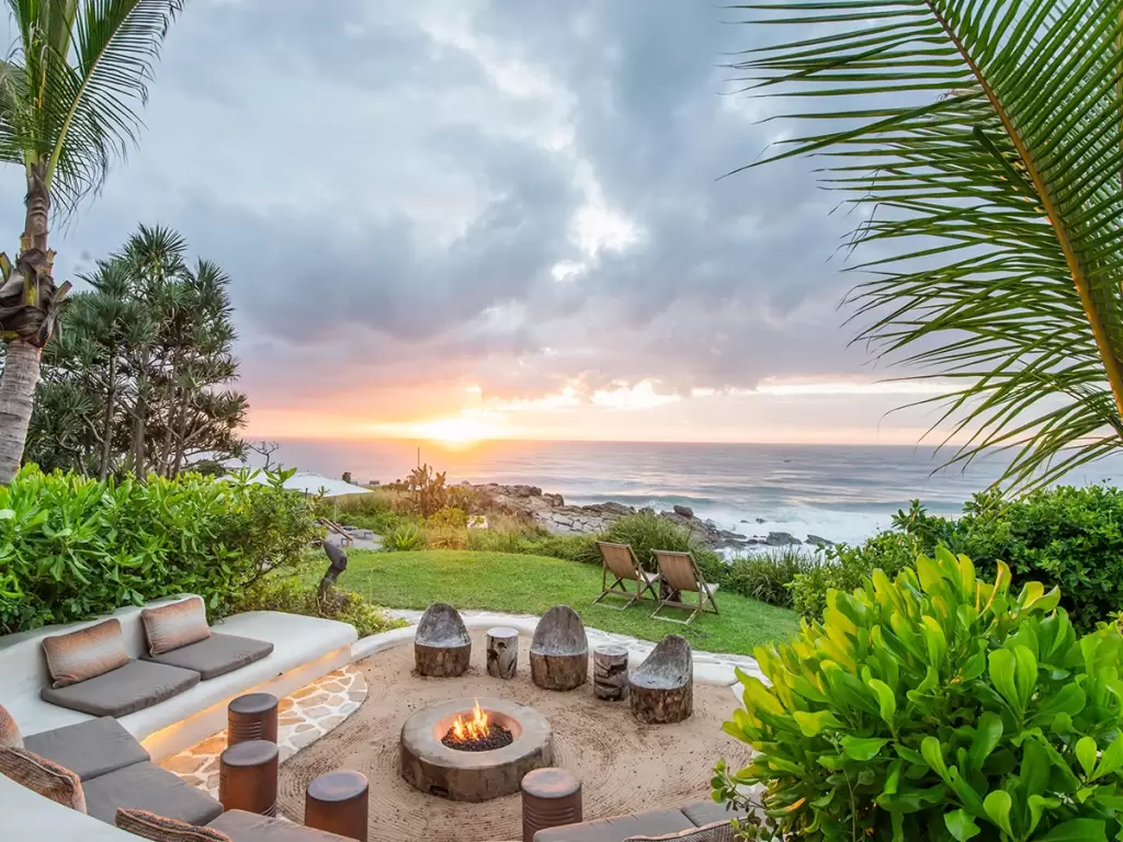 A cinematic view of luxury oceanfront fire pit and lounge at sunset on South Africa’s coast. 